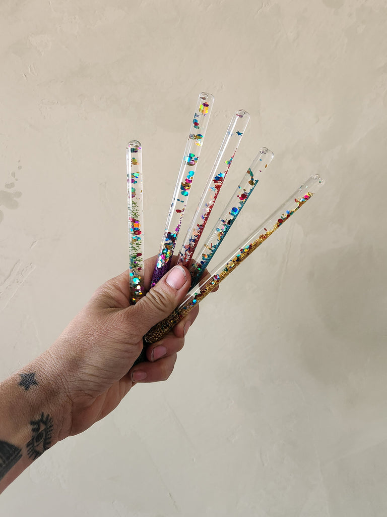 A hand holding a variety of small wands filled with multi colored glitter.