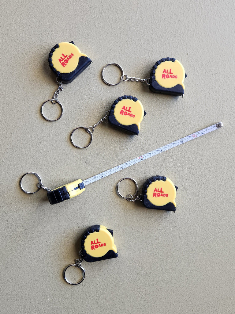 black and yellow mini tape measure with All Roads logo keychain.